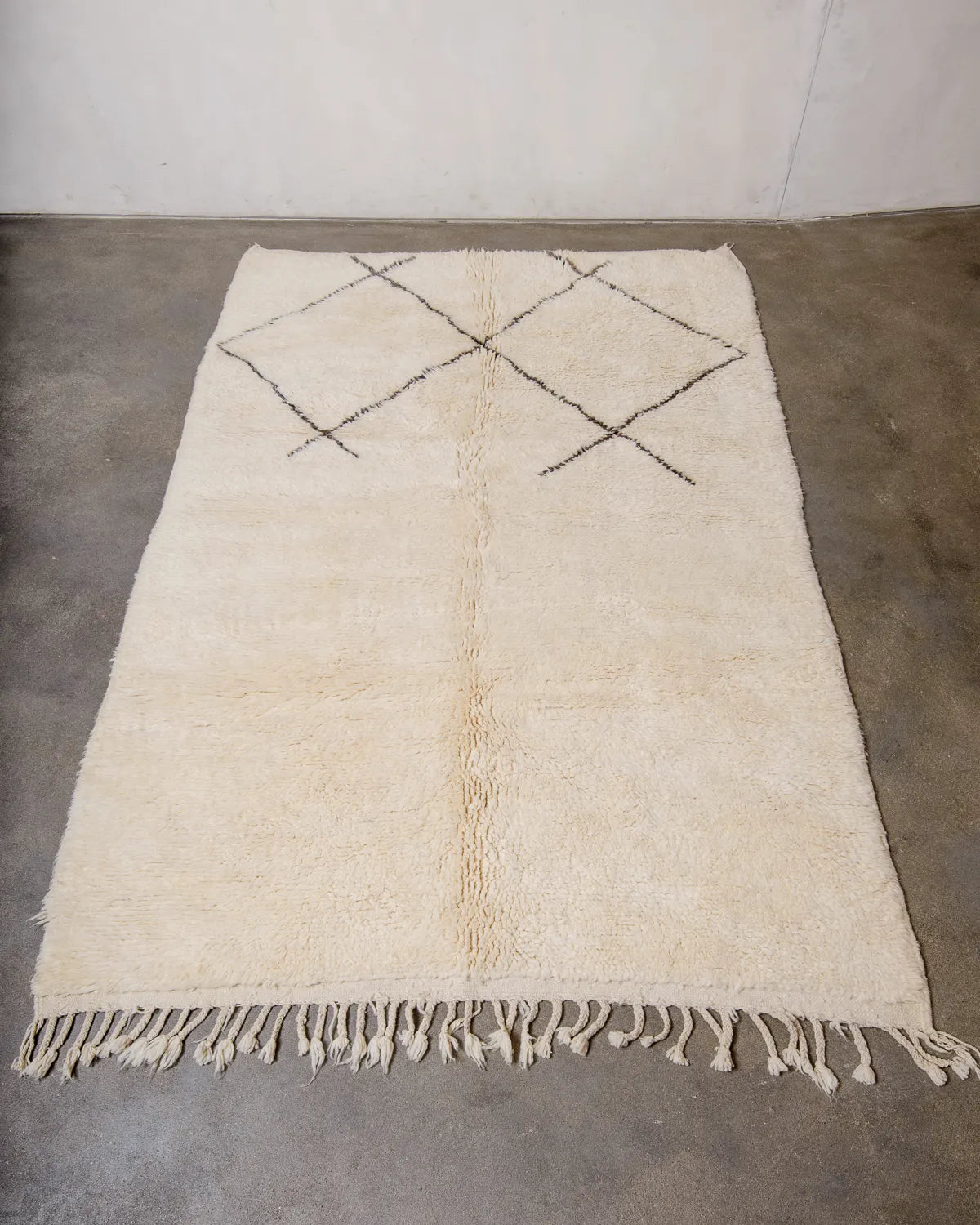 Vintage wool Berber rug from Morocco in cream wool and minimal grey-brown line design, laying flat on concrete floor.